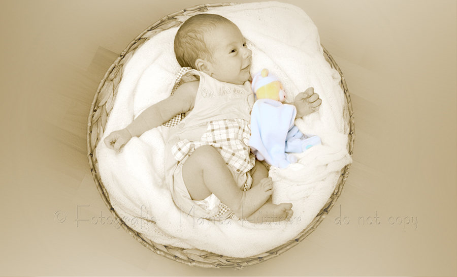 ein neugeborenes Baby liegt lächelnd in einem runden Korb - Sepiafoto mit Farbe