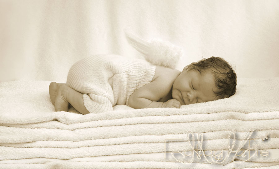 Neugeborenes Baby mit kleinen Engelsflügeln auf einem Stapel Handtücher.