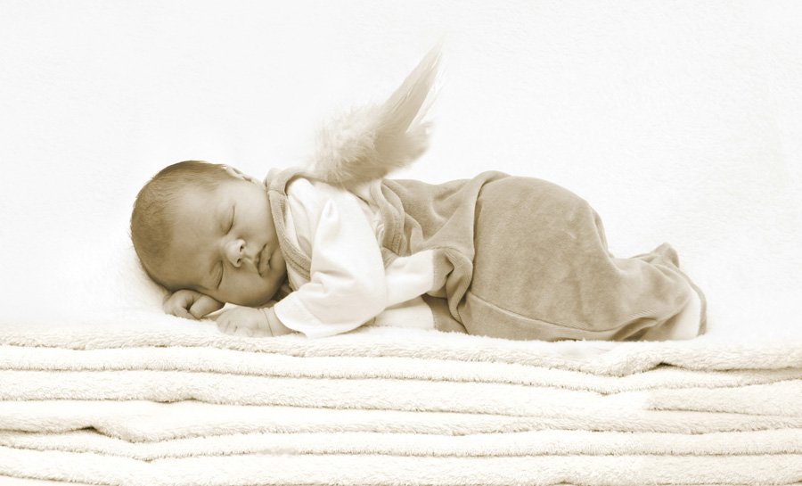 neugeborenes Baby mit kleinen Engelsflügeln liegt auf einem Stapel Handtüchern