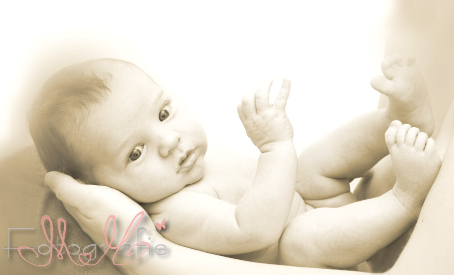 Eine Sepia-Fotografie von einem kleinen nackten Baby auf Mamas Schoß.