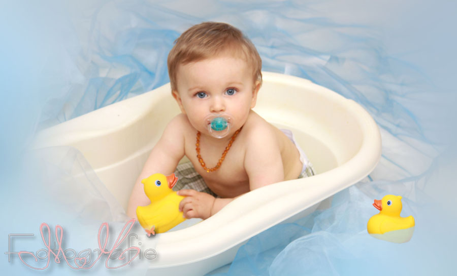 Foto von einem Kleinkind in einer weißen Badewanne, drumherum blaue Dekotücher.