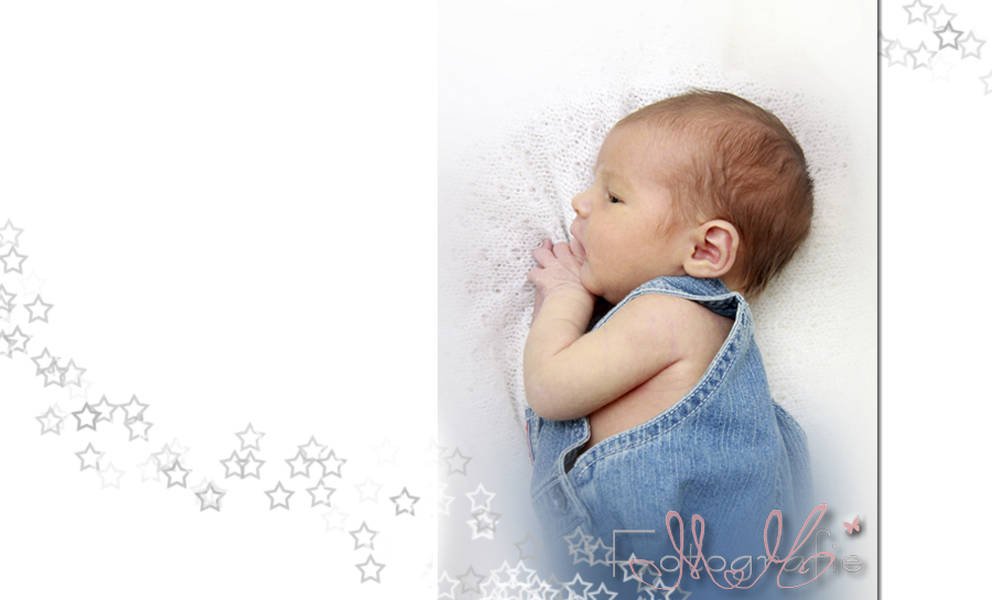 Ein kleines Baby liegt auf der Seite auf einer weißen Wolldecke, es trägt eine blaue Latzhose.