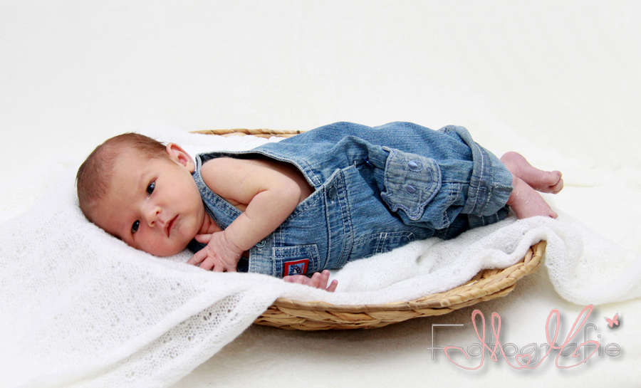 Fotografie eines ganz kleinen Neugeborenen mit einer blauen Latzhose an.