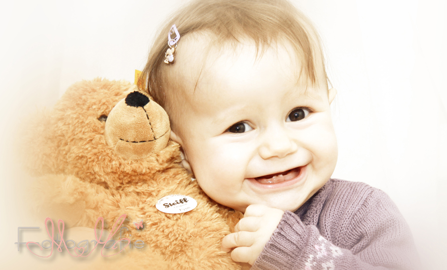 Lachendes Baby mit einem braunen Teddybär.