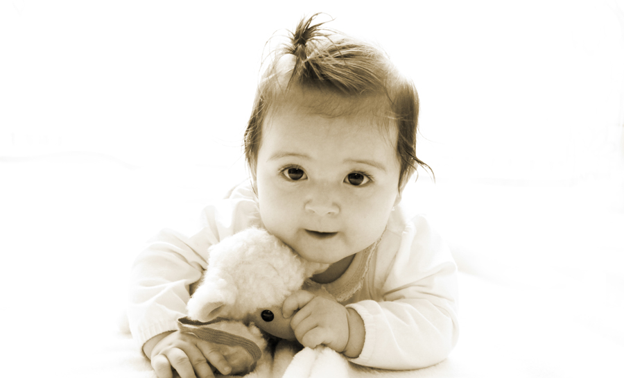 Sepia-Aufnahme eines Babys das auf dem Bauch liegt mit einem Kuscheltier.
