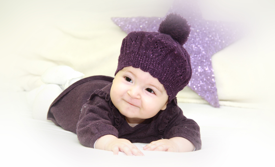 Baby liegt auf dem Bauch, auf dem Kopf eine lila Mütze, im Hintergrund ein lila Stern.
