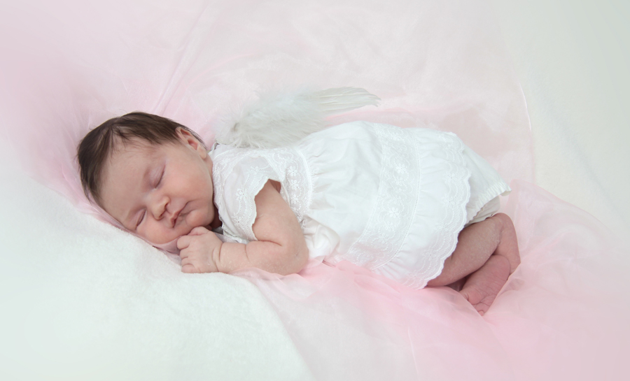 Ein kleines neugeborenes Mädchen liegt auf einer rosa Decke mit kleinen Engelsflügeln