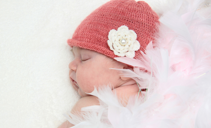 kleines Baby mit rosa Mütze und weißer Häkelblume