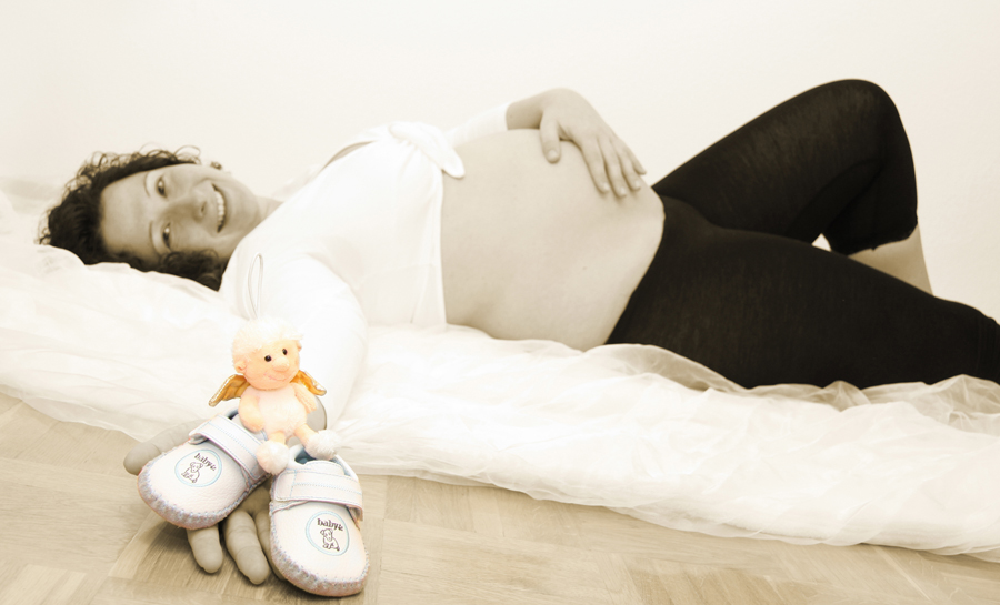 Schwangere Frau zeigt Babyschuhe